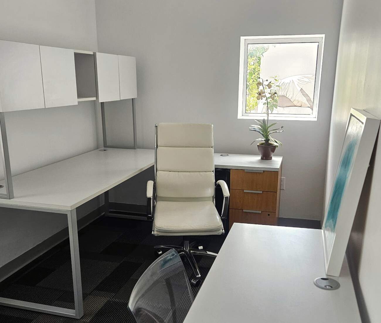 A private office with a desk, a white chair and a window onto greenery